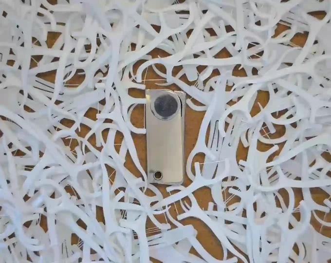 A closed Flossr surrounded by many white disposable floss picks.